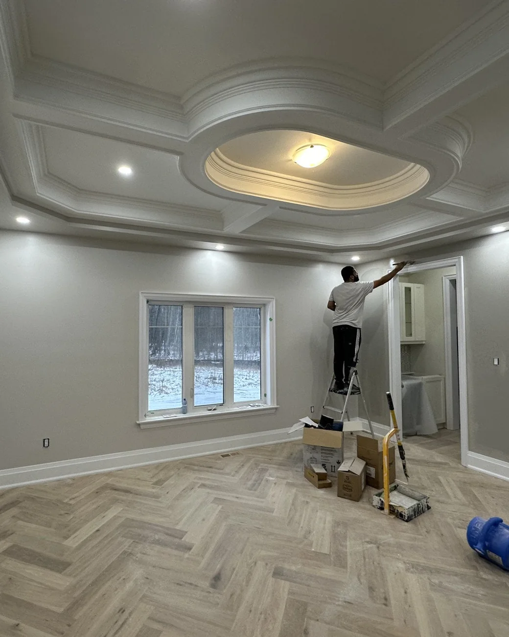 G & M Painting painter finishing the walls of a custom home with a coffered ceiling and herringbone floor