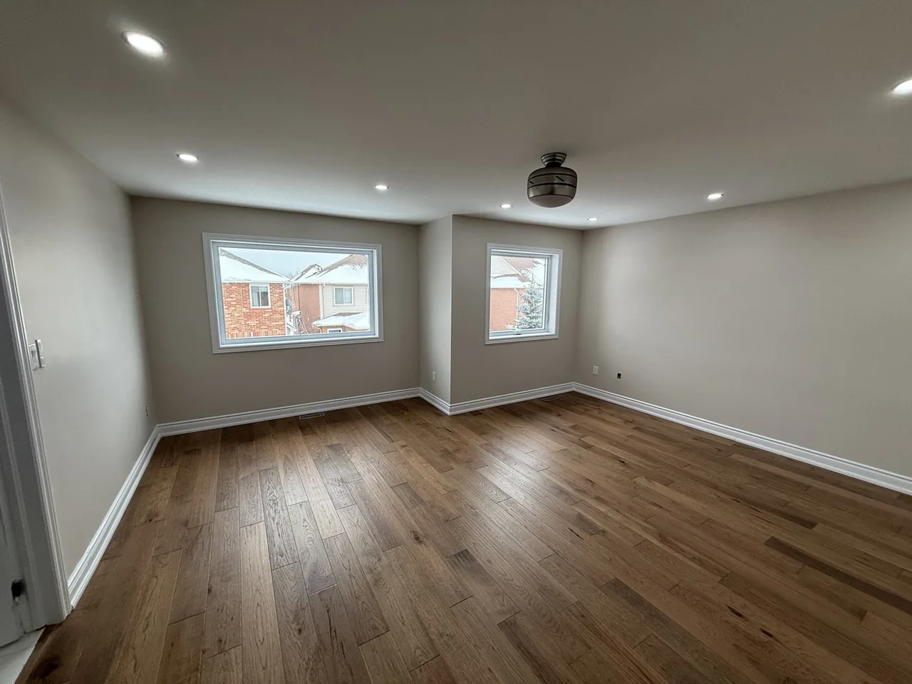 Freshly painted bright interior room with two windows and hardwood floor